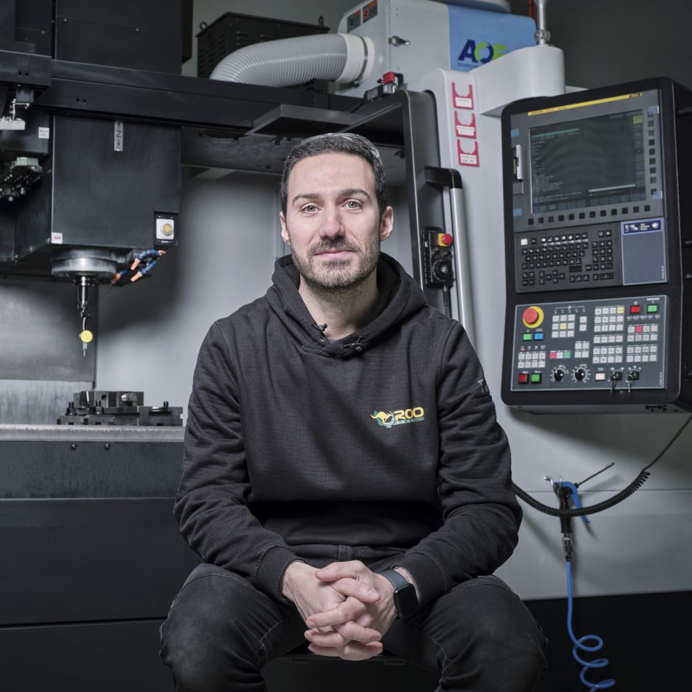 A focused machine operator posing in front of advanced machinery with a control panel in the background.